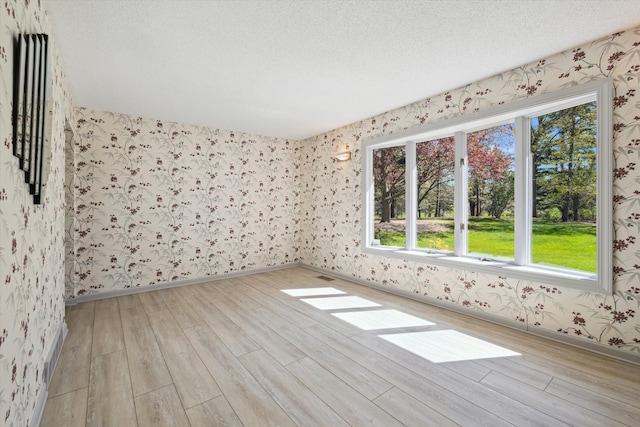 spare room featuring plenty of natural light, wallpapered walls, light wood-type flooring, and a textured ceiling