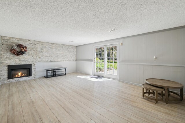 living room featuring a textured ceiling, visible vents, a fireplace, wood finished floors, and a wainscoted wall