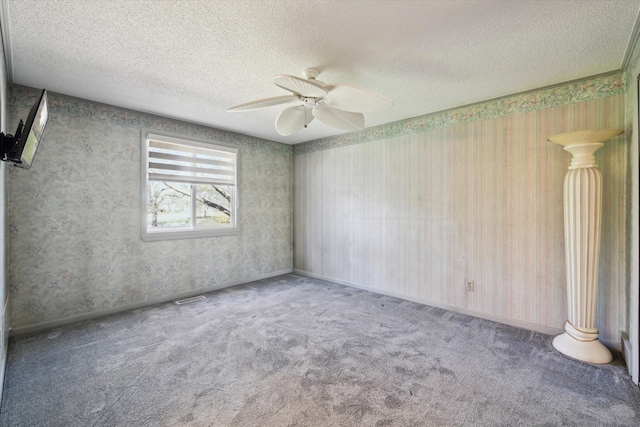 empty room with carpet flooring, ceiling fan, a textured ceiling, wallpapered walls, and visible vents