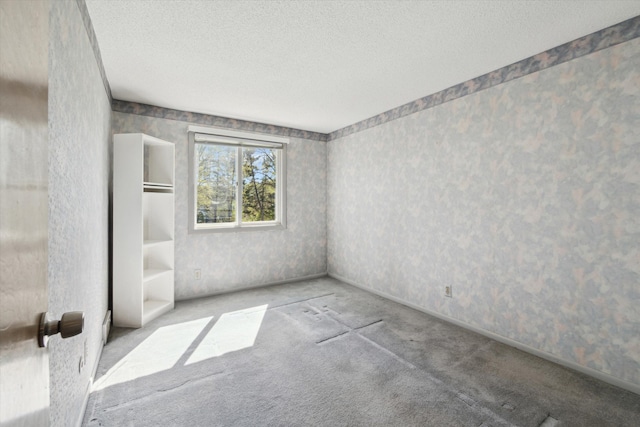 empty room with carpet, a textured ceiling, and wallpapered walls