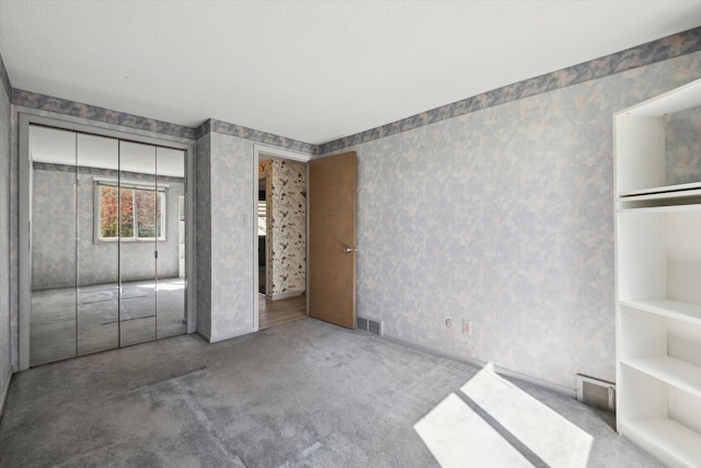 unfurnished bedroom with a closet, carpet, visible vents, and wallpapered walls