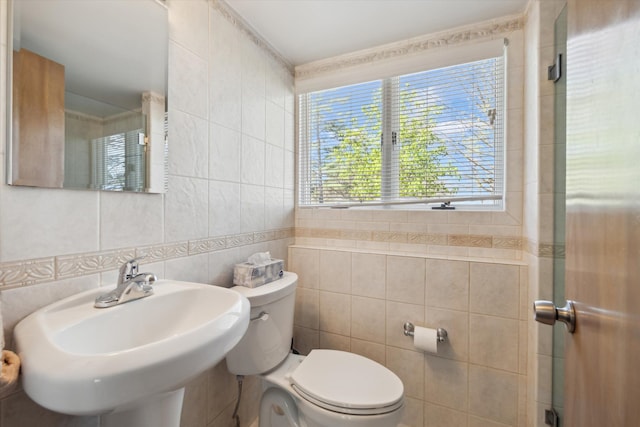 bathroom with a sink, tile walls, and toilet