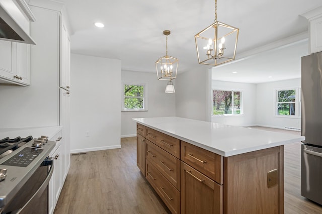 kitchen with wall chimney range hood, light wood-style floors, stainless steel appliances, and a wealth of natural light