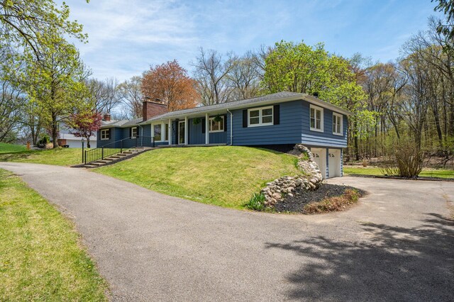 single story home with an attached garage, a chimney, driveway, and a front yard
