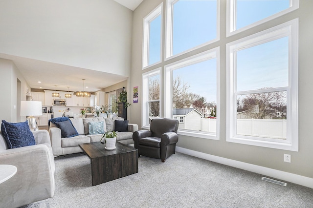 living area featuring a towering ceiling, baseboards, light carpet, and visible vents