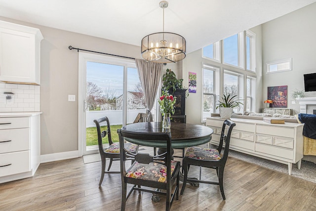dining space with baseboards, an inviting chandelier, light wood finished floors, and a fireplace