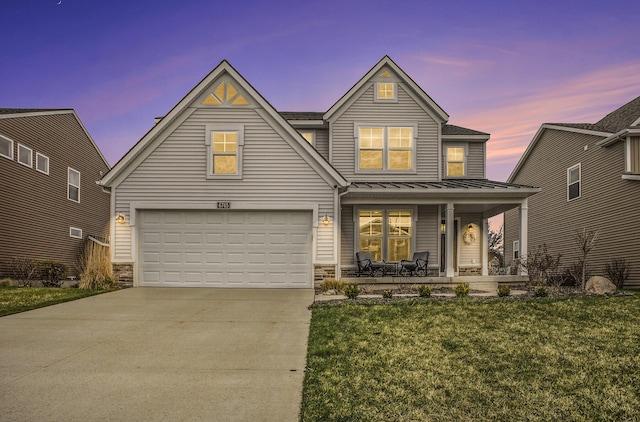 traditional-style home with a front lawn, stone siding, a standing seam roof, concrete driveway, and a porch