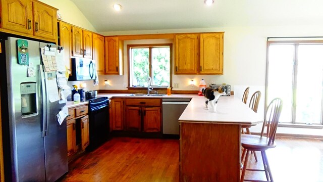 7407 Beecher Rd, Flint, MI 48532 - kitchen with appliances with stainless steel finishes, a peninsula, brown cabinetry, a kitchen bar, and lofted ceiling