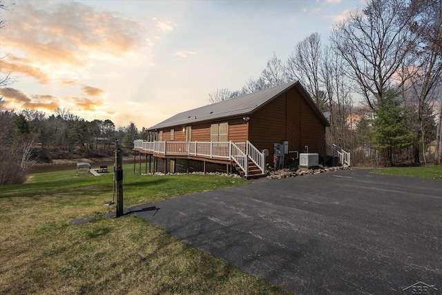 back of property at dusk with a lawn, central AC unit, a deck, and metal roof