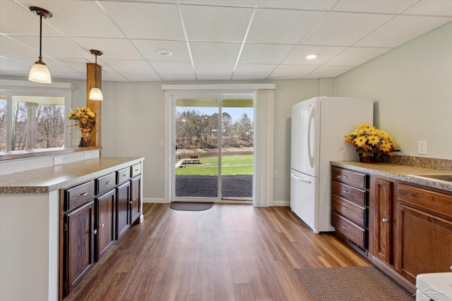 kitchen with pendant lighting, freestanding refrigerator, a drop ceiling, and dark wood-style floors
