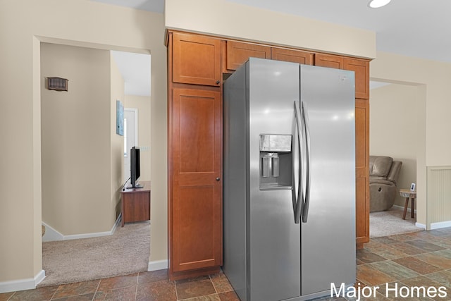 kitchen with stainless steel refrigerator with ice dispenser, baseboards, stone finish flooring, and brown cabinetry