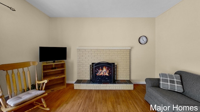 living area with a brick fireplace, baseboards, and wood finished floors