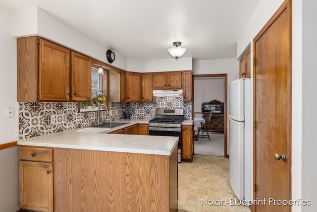 kitchen featuring gas stove, a sink, freestanding refrigerator, a peninsula, and under cabinet range hood