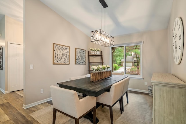 dining room with light wood-style floors, baseboards, an inviting chandelier, and vaulted ceiling