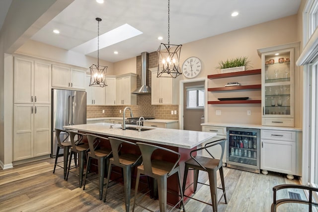 kitchen featuring wall chimney range hood, a chandelier, wine cooler, a breakfast bar, and high end fridge