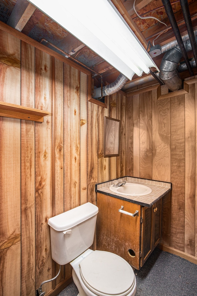 bathroom featuring vanity, wood walls, and toilet