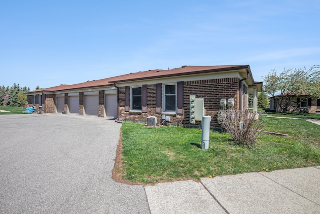 view of front of house with brick siding, central AC, community garages, and a front lawn