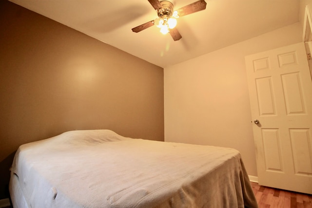 bedroom featuring a ceiling fan, baseboards, vaulted ceiling, and wood finished floors