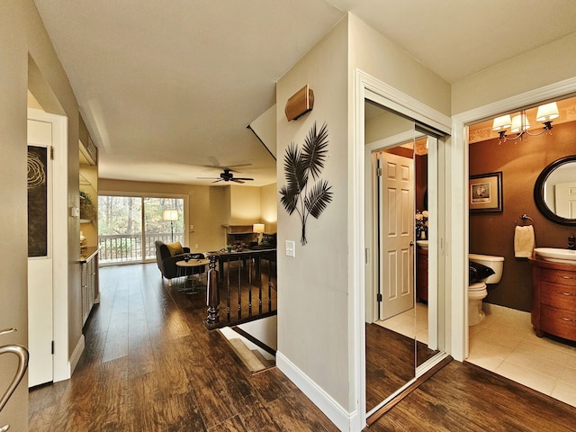 corridor featuring an inviting chandelier, a sink, baseboards, and wood finished floors