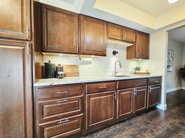kitchen featuring tasteful backsplash, light stone countertops, a sink, baseboards, and dark wood-type flooring