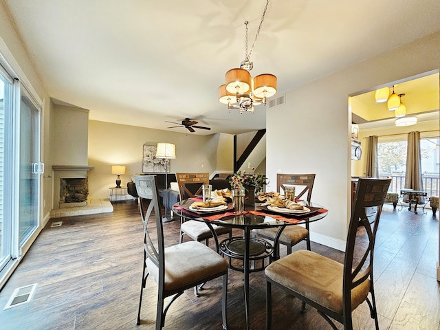 dining room with visible vents, a large fireplace, wood finished floors, baseboards, and ceiling fan with notable chandelier