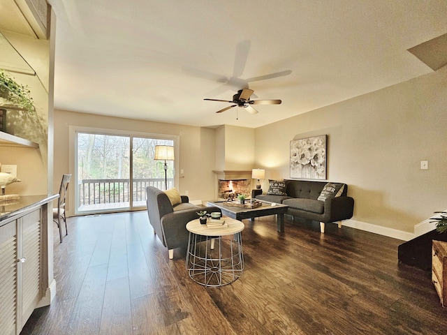 living area featuring a ceiling fan, baseboards, a lit fireplace, and wood finished floors