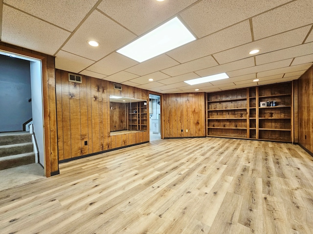 finished basement with wooden walls, built in shelves, light wood finished floors, and stairway