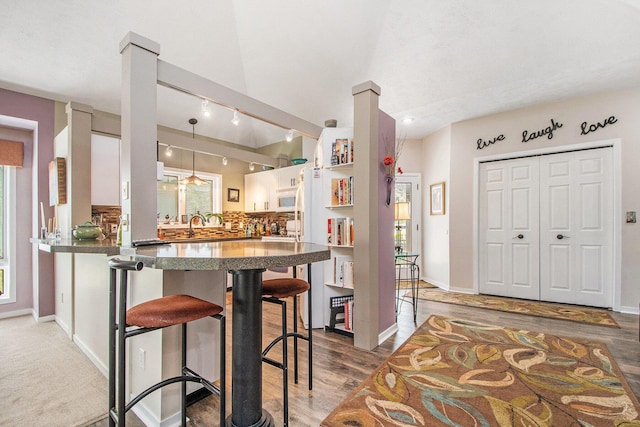 kitchen with a breakfast bar area, light wood-type flooring, baseboards, white cabinets, and a peninsula
