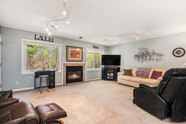 living room featuring track lighting, baseboards, a tiled fireplace, and light colored carpet