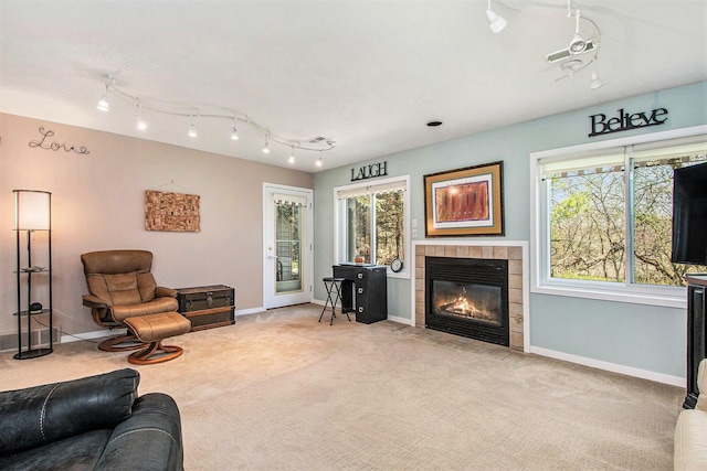 living room featuring carpet floors, rail lighting, a tiled fireplace, and baseboards