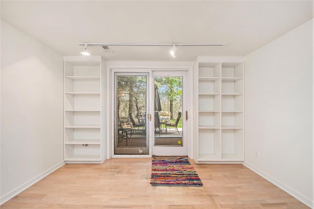 doorway to outside with baseboards, rail lighting, wood finished floors, and built in shelves