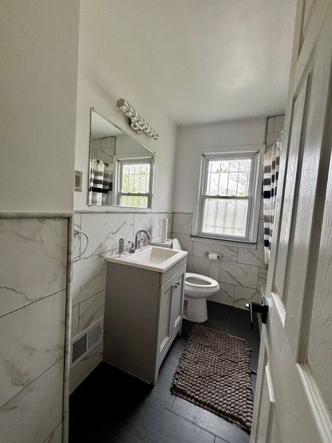 full bathroom featuring vanity, wainscoting, wood finished floors, toilet, and tile walls