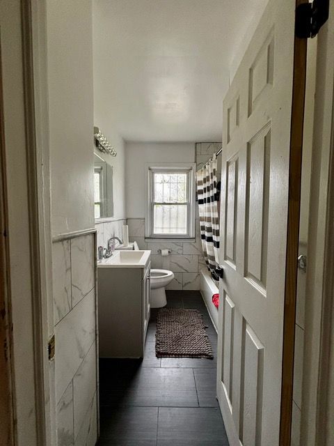 full bathroom with a shower with curtain, tile walls, wainscoting, vanity, and toilet