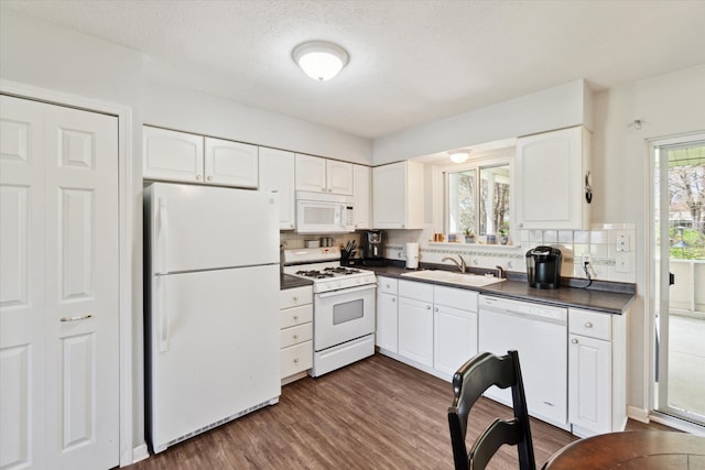 kitchen featuring white appliances, backsplash, dark countertops, and a sink