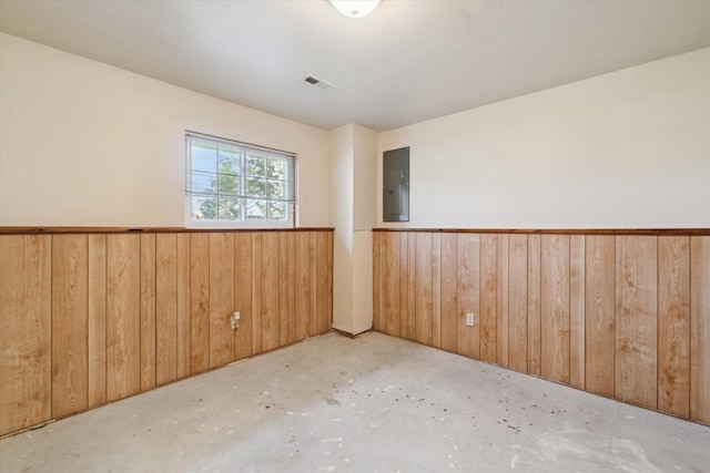 empty room featuring visible vents, wood walls, wainscoting, electric panel, and concrete floors
