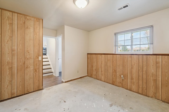 unfurnished bedroom featuring wood walls, concrete floors, and visible vents