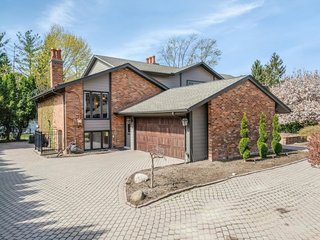 tri-level home with a shingled roof, brick siding, a garage, a chimney, and decorative driveway