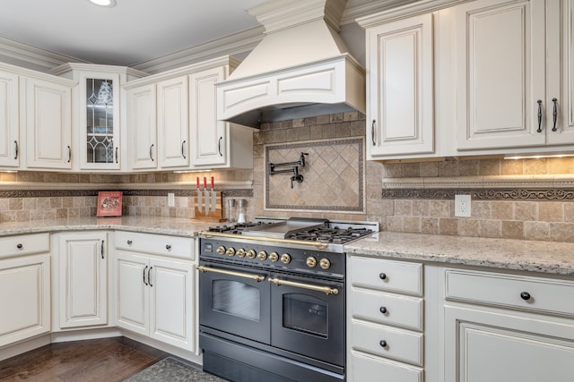 kitchen with white cabinetry, double oven range, custom range hood, tasteful backsplash, and glass insert cabinets