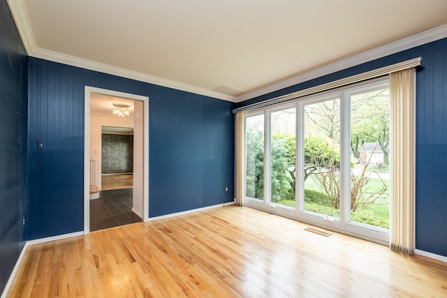 empty room featuring ornamental molding, healthy amount of natural light, wood finished floors, and baseboards