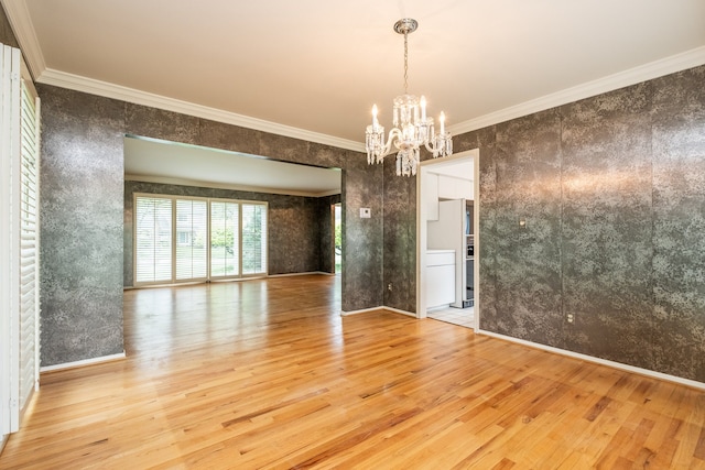 spare room with wood finished floors, a chandelier, crown molding, and baseboards