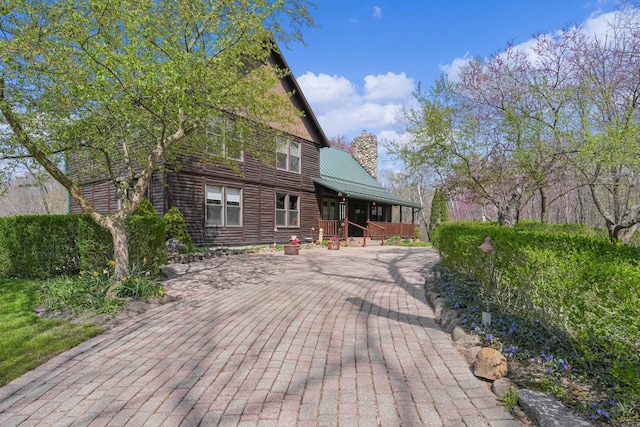 rear view of property featuring covered porch, a standing seam roof, a chimney, and metal roof