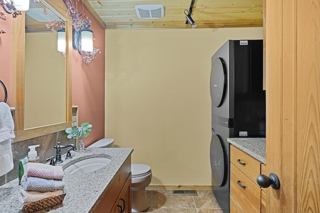 half bathroom with stacked washer and dryer, visible vents, vanity, baseboards, and toilet