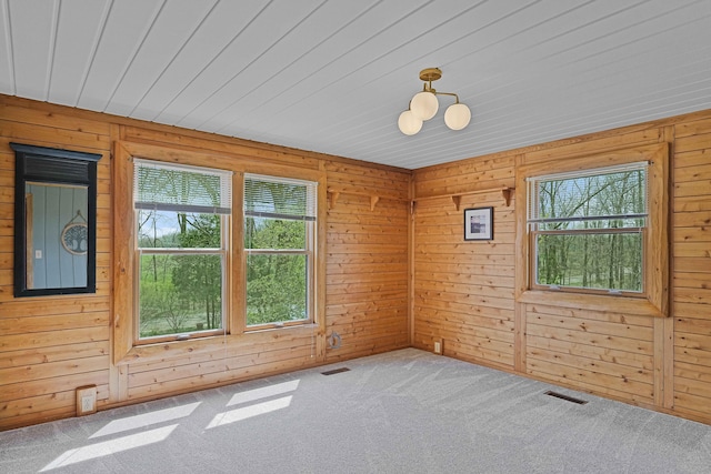 carpeted spare room with wooden walls, visible vents, and a wealth of natural light