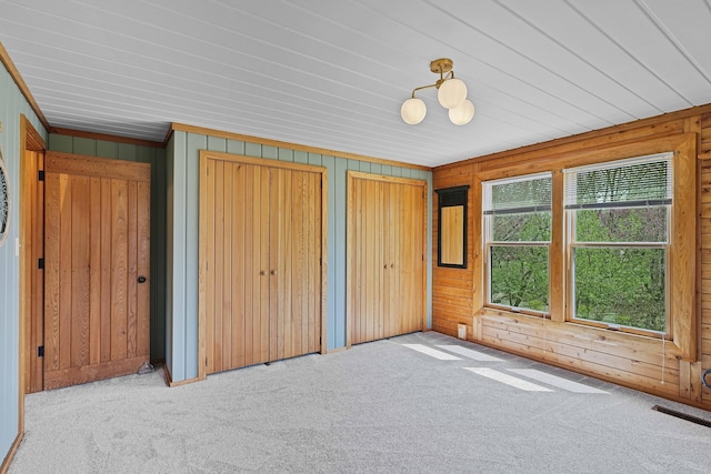 unfurnished bedroom with visible vents, carpet flooring, multiple closets, and wooden walls