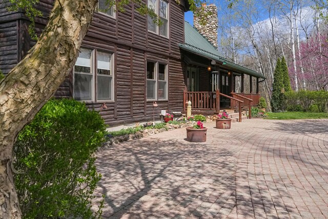 exterior space featuring faux log siding, a chimney, a patio area, and metal roof