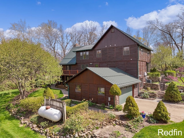 view of home's exterior featuring a garage, metal roof, a chimney, a standing seam roof, and concrete driveway