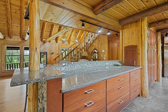 kitchen featuring wood ceiling, wood walls, rail lighting, beam ceiling, and dark stone counters