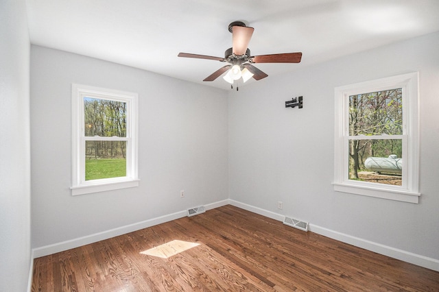 spare room with visible vents, dark wood-style floors, ceiling fan, and a wealth of natural light