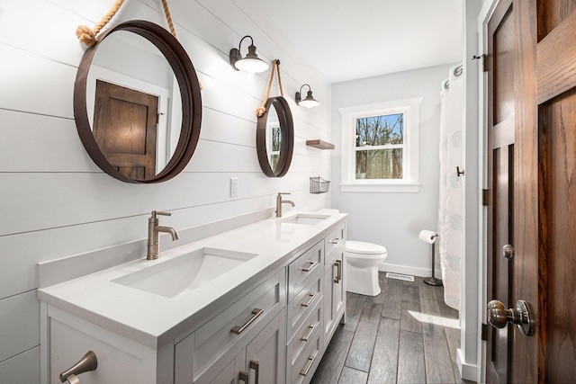 full bathroom with a sink, double vanity, toilet, and wood finished floors