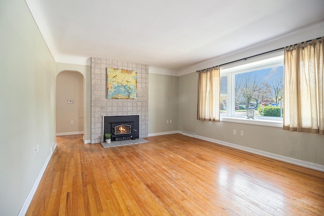 unfurnished living room featuring baseboards, arched walkways, and light wood finished floors